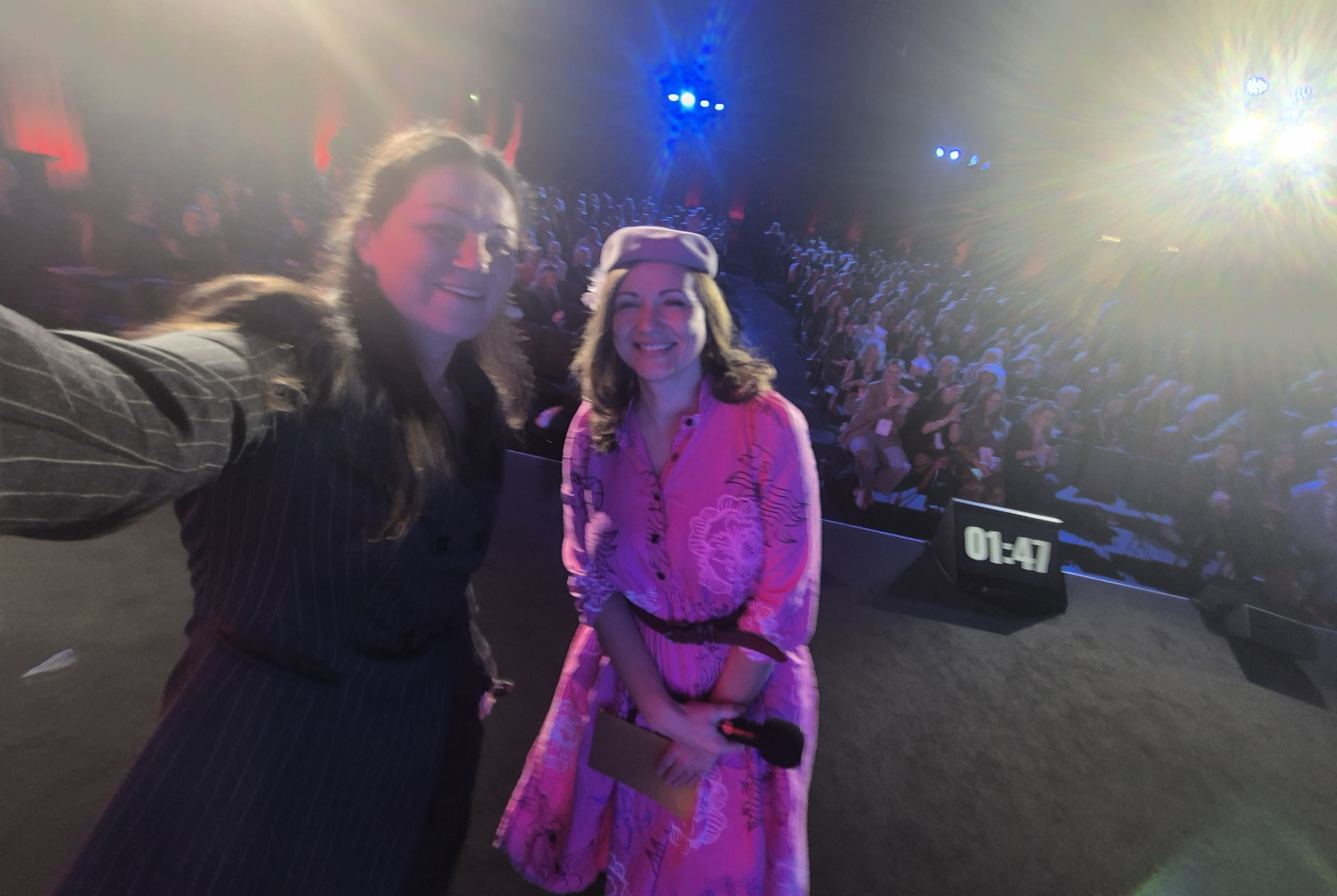 Ieva Drāzniece uz skatuvas kopā ar kolēģi, aiz mugras pilna auditorija
